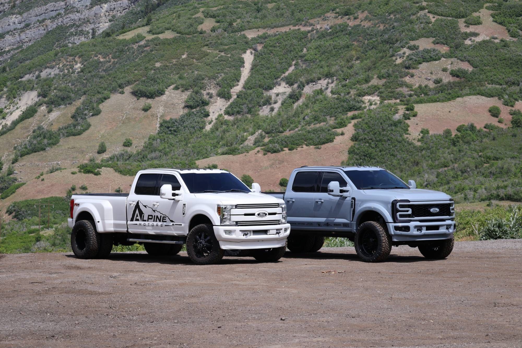 Two lifted Ford Super Duty dually trucks from Alpine Motors in front of the mountains near Provo, Utah